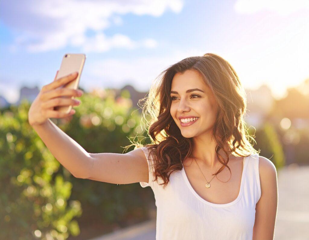 A cheerful woman smiling in sunlight while taking a selfie, representing positivity and happiness — perfect for the blog post “Smile Captions for Instagram.”